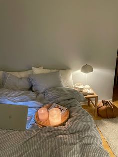 a laptop computer sitting on top of a bed next to a night stand and lamp