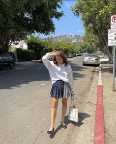 a woman walking down the street with her hand on her head and holding a purse