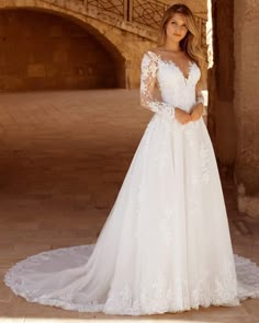 a woman in a white wedding dress standing on a stone walkway with an archway behind her