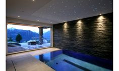 an indoor swimming pool in the middle of a living room with large windows and stone walls