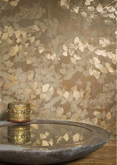 a glass bowl on a wooden table in front of a wall with gold leaf designs