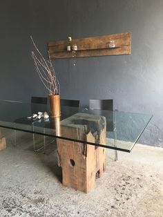 a glass table with a wooden base and vase sitting on it's side in front of a gray wall