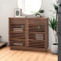 a wooden cabinet sitting on top of a hard wood floor next to a potted plant