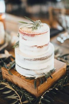 a three tiered wedding cake with rosemary sprigs on top sits on a wooden table