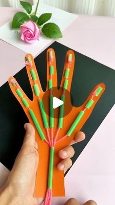 someone is holding up an orange and green paper hand with four different colored pens in it