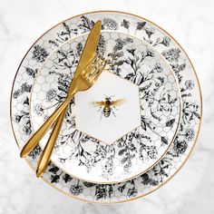 a plate with a bee on it next to a gold fork and knife, sitting on a marble table