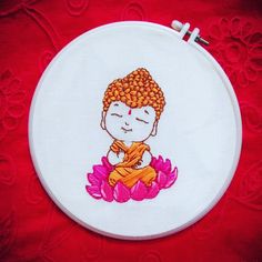 a little buddha sitting on top of a pink flower in front of a white embroidery hoop