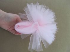 a hand is holding a pink and white tulle hair clip on a beige surface