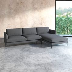 a gray couch sitting in front of a window next to a concrete wall and floor