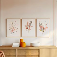 three paintings on the wall above a wooden cabinet with a bowl and vase in front of it