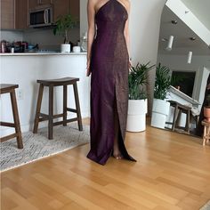 a woman in a purple dress standing on a hard wood floor next to a plant