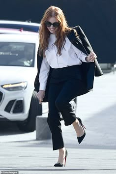 a woman in black pants and white shirt walking down the street