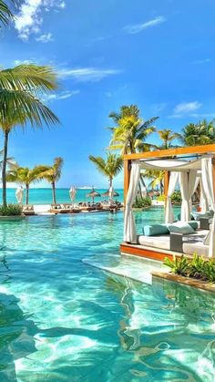 an outdoor swimming pool with cabanas and palm trees on the beach in front of it