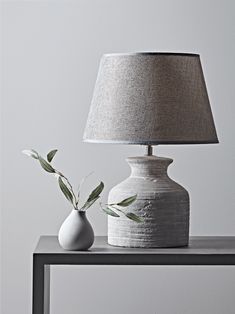 a white vase sitting on top of a wooden table next to a lampshade