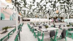 an outdoor dining area with tables, benches and hanging plants on the ceiling above them