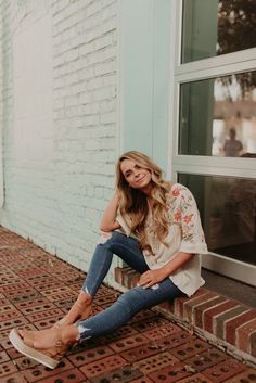 a woman sitting on the ground in front of a brick building with her legs crossed