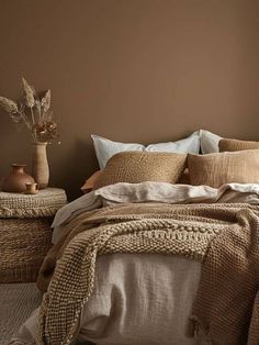 a bed with pillows and blankets on it in front of a brown wall next to a window