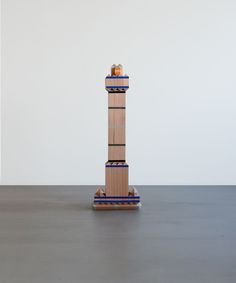 a tall wooden tower sitting on top of a gray floor next to a white wall