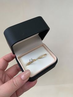 a hand holding an open ring box with a diamond in it and the lid opened