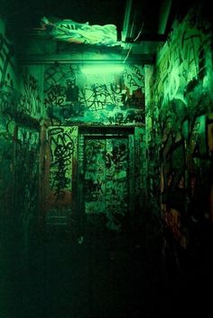 a dark room with graffiti all over the walls and door to another room that is covered in green light