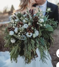 a bride and groom are kissing in front of the camera with pine cones on their bouquet