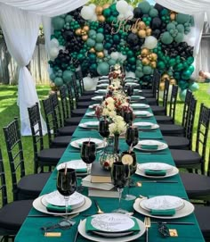 a long table is set with black and white plates, green napkins, and balloons