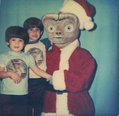 two young boys standing next to a large stuffed animal wearing a santa claus hat and holding hands