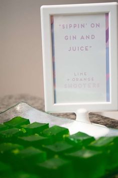 a white frame sitting on top of a table filled with green jellos next to a sign that reads sippin'on gin and juice