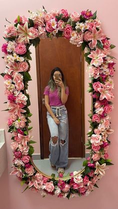 a woman taking a selfie in front of a mirror with pink flowers around it