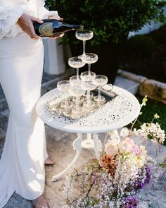 a woman in white dress pouring champagne into wine glasses on a table with flowers and greenery