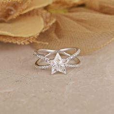 a white gold ring with a star shaped diamond in the center on a beige background