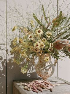 a vase filled with lots of flowers sitting on top of a table next to a wall