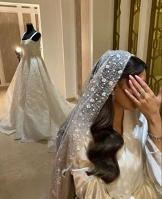 the bride is covering her face while looking at herself in front of a wedding dress