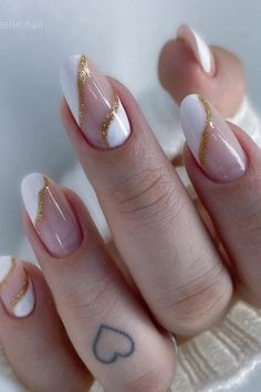 a woman's hand with white and gold manies on her nails, holding a heart