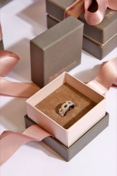 an open box with a wedding ring in it and pink ribbon on the floor next to it