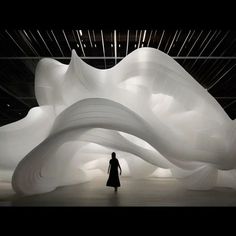 a woman is standing in front of a large white sculpture that looks like it's floating