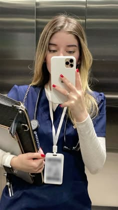 a woman in scrubs takes a selfie with her cell phone while holding a folder