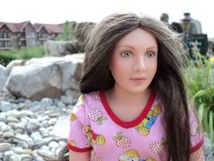 a doll with long hair is standing in front of some rocks and flowers on the ground