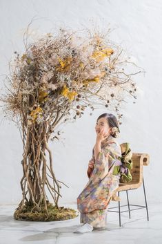 a woman sitting on a chair in front of a tree with branches and flowers growing out of it