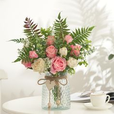 a vase filled with pink and white flowers on top of a table next to a cup