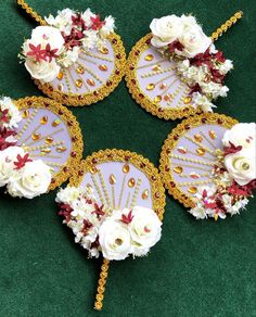 four fan shaped decorations with white flowers and gold trimmings on a green surface