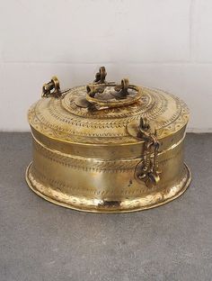 an antique brass box with birds on it sitting on the floor next to a white wall