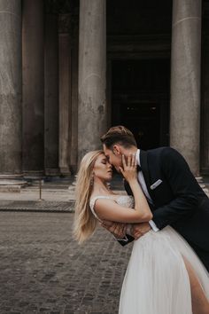 a bride and groom kissing in front of an old building with columns on either side