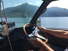 a man driving a truck down a road next to a lake with mountains in the background