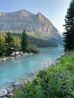 a river running through a lush green forest covered hillside next to a tall mountain range