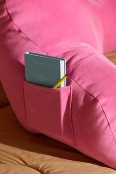 a pink couch with a book in it's pocket on top of the pillow