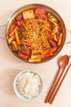 a pan filled with food next to rice and chopsticks