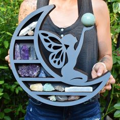 a woman holding up a metal plaque with rocks and crystals in it's center