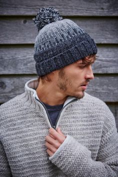 a man wearing a grey sweater and a gray hat with a pom - pom