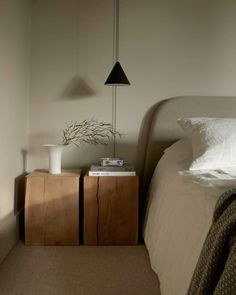 a white bed sitting next to a wooden night stand with a lamp on top of it